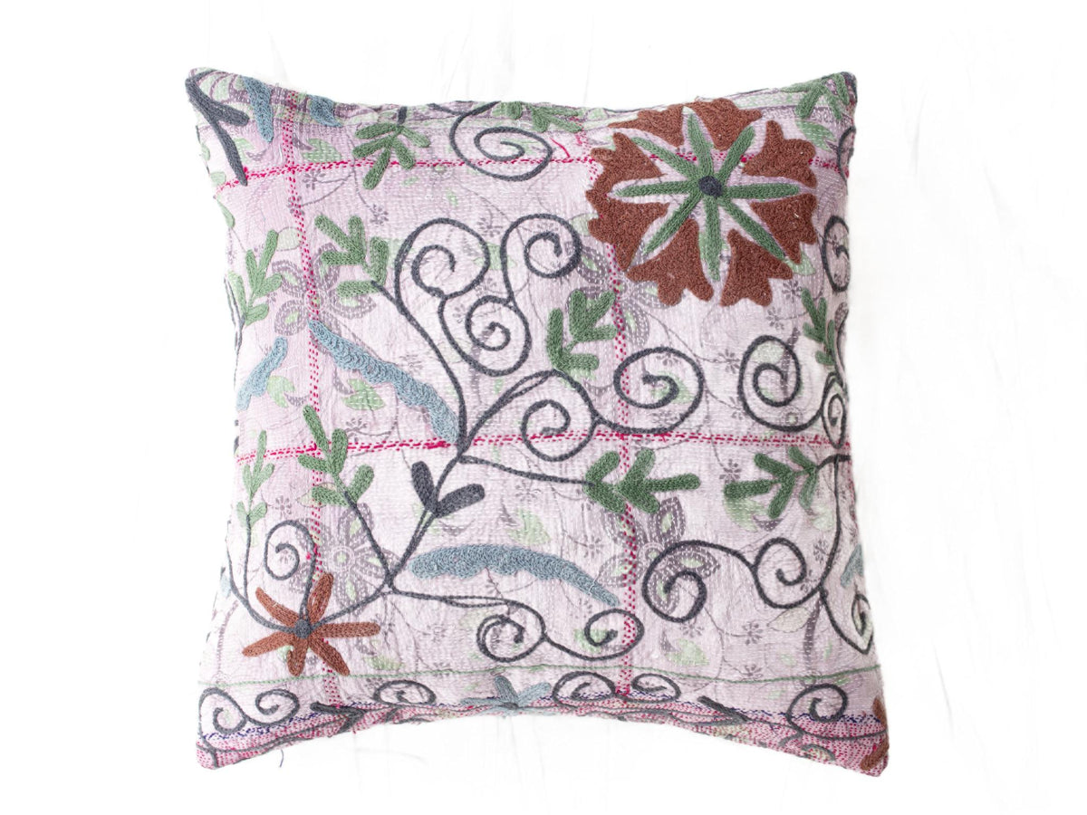 Unique suzani pillowcase 50x50 with white base and colorful embroidered flowers as well as green leaves and black sling ornaments in boho vintage style.